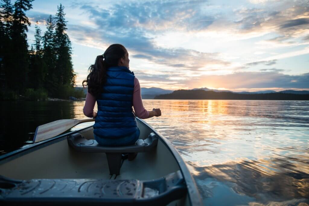 woman paddles canoe on lake at sunset