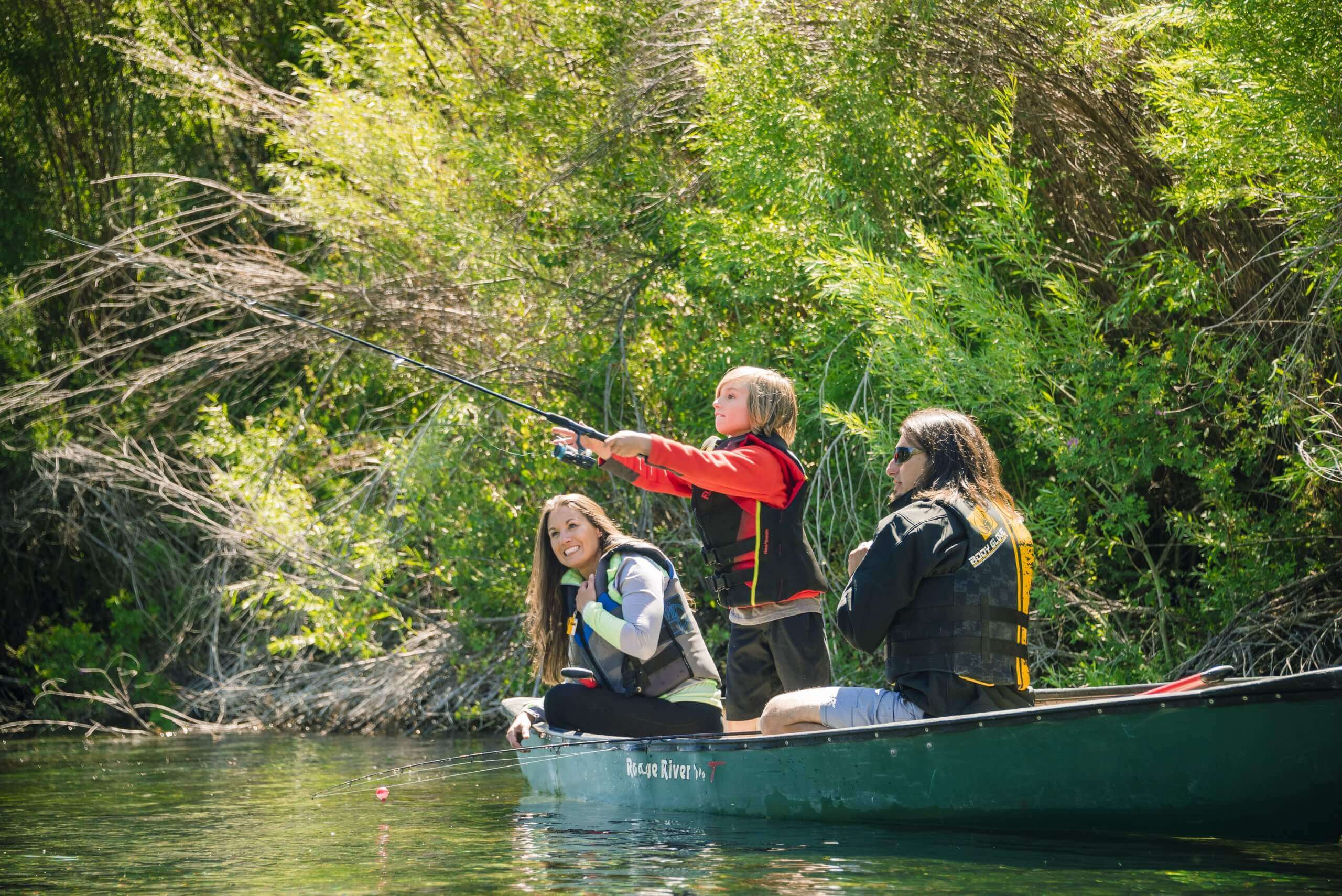A group of three people fishing from a canoe on a tree-lined river at Thousand Springs State Park.