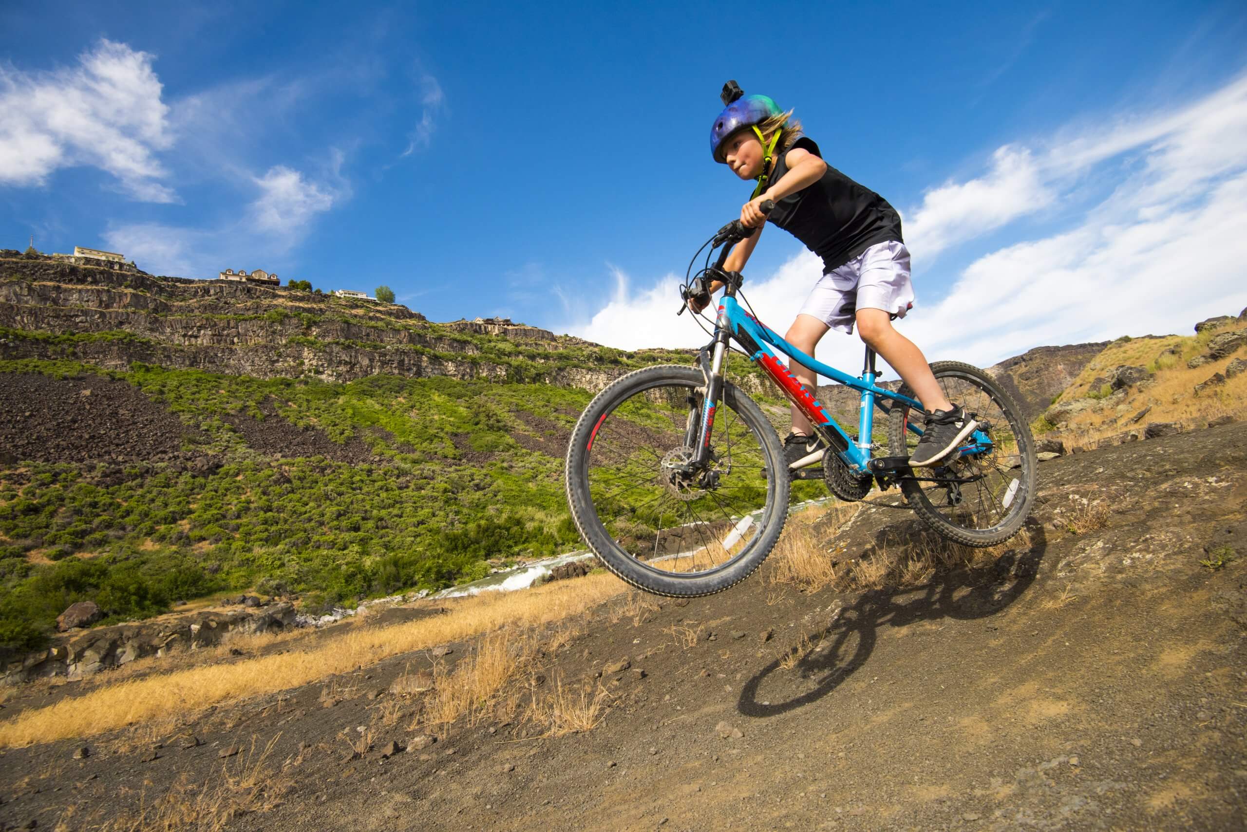 A child on a mountain bike in mid jump, going down a dirt trail surrounded by canyon walls in Snake River Canyon.