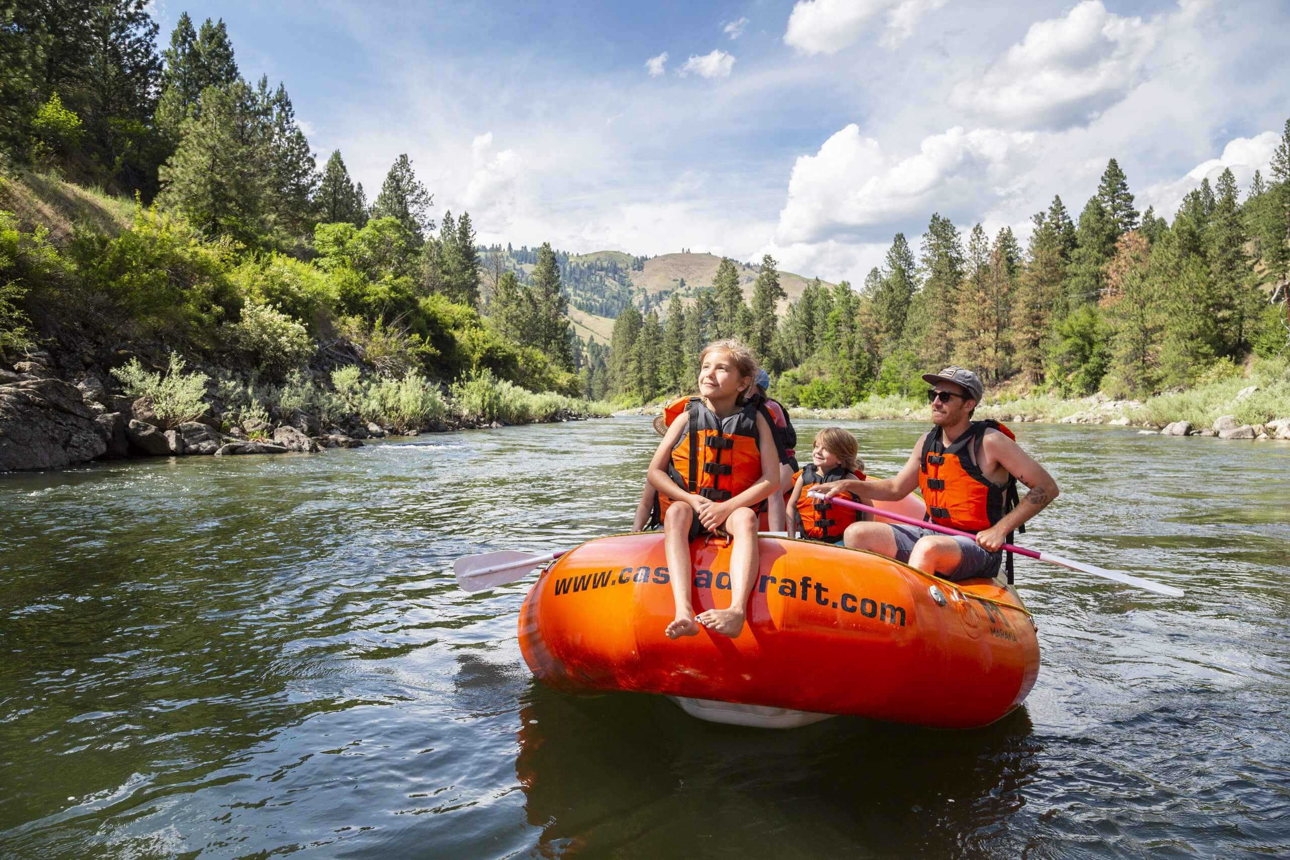 A family rafting on the Payette River surrounded by a forest of trees.