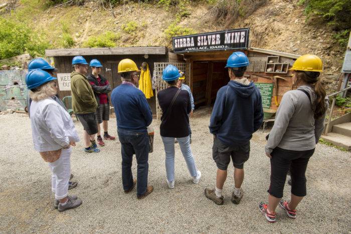 a group of people, all wearing hard hats, wait outside a mine entrance