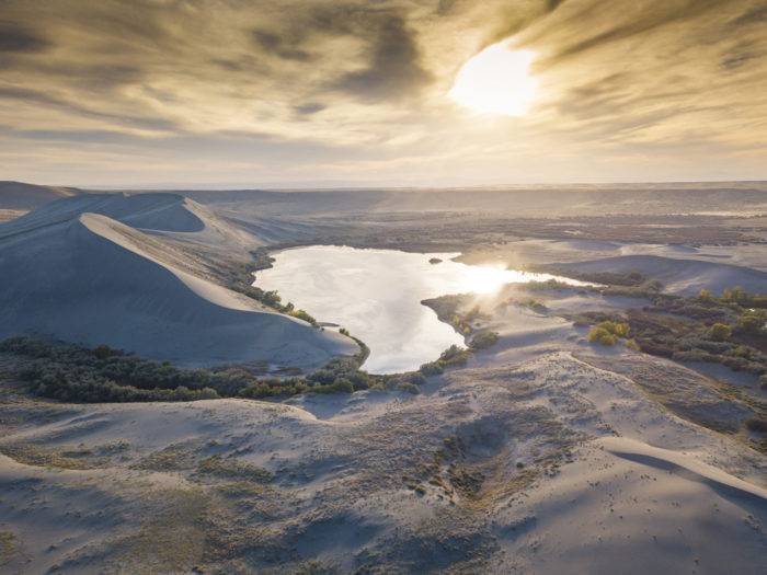 Wide shot of sand dunes and a body of water at sunrise at Bruneau Dunes State Park.