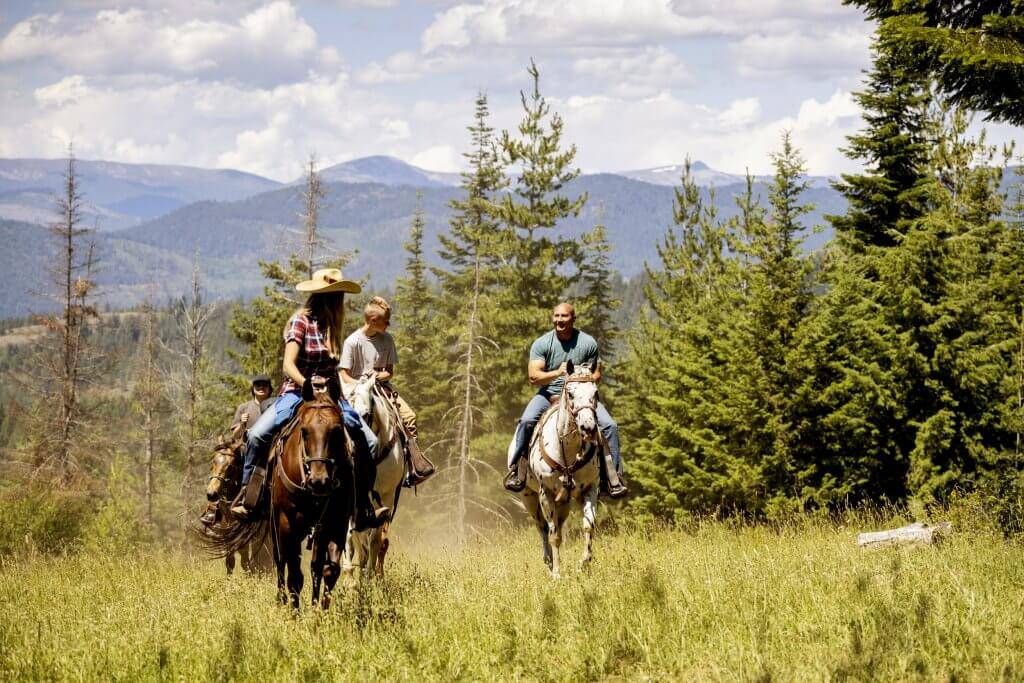 Three people riding horseback through a lush meadow at Western Pleasure Guest Ranch.