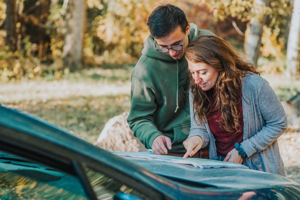a couple reading a map that's spread out on the hood of a car