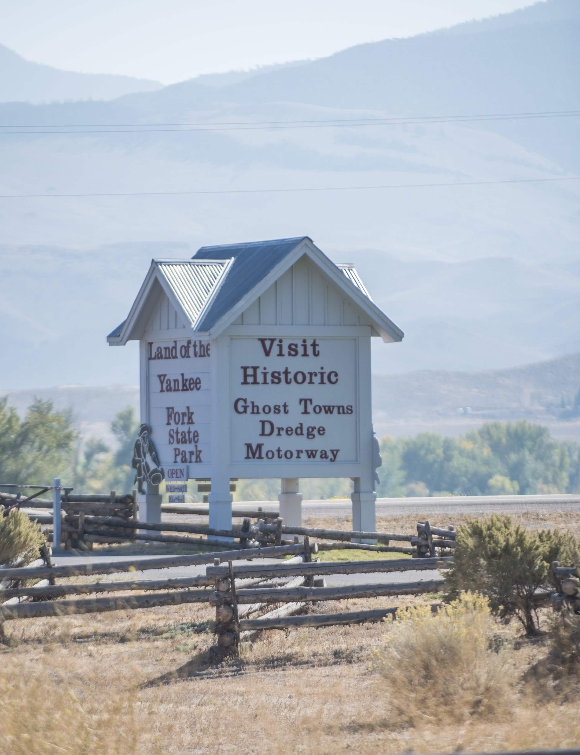 A white, wooden, house-shaped sign that reads "Land of the Yankee Fork State Park" on one side and "Visit Historic Ghost Towns Dredge Motorway" on the other.