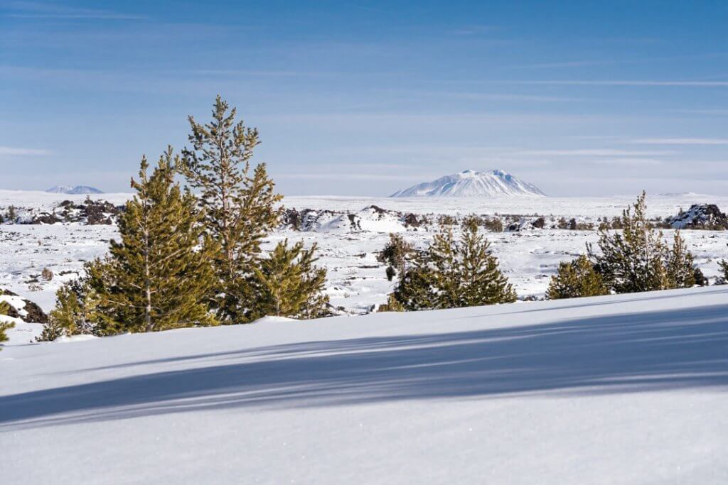 A view of the snow-covered landscapes and a cinder cone in the distance at Craters of the Moon National Monument & Preserve.