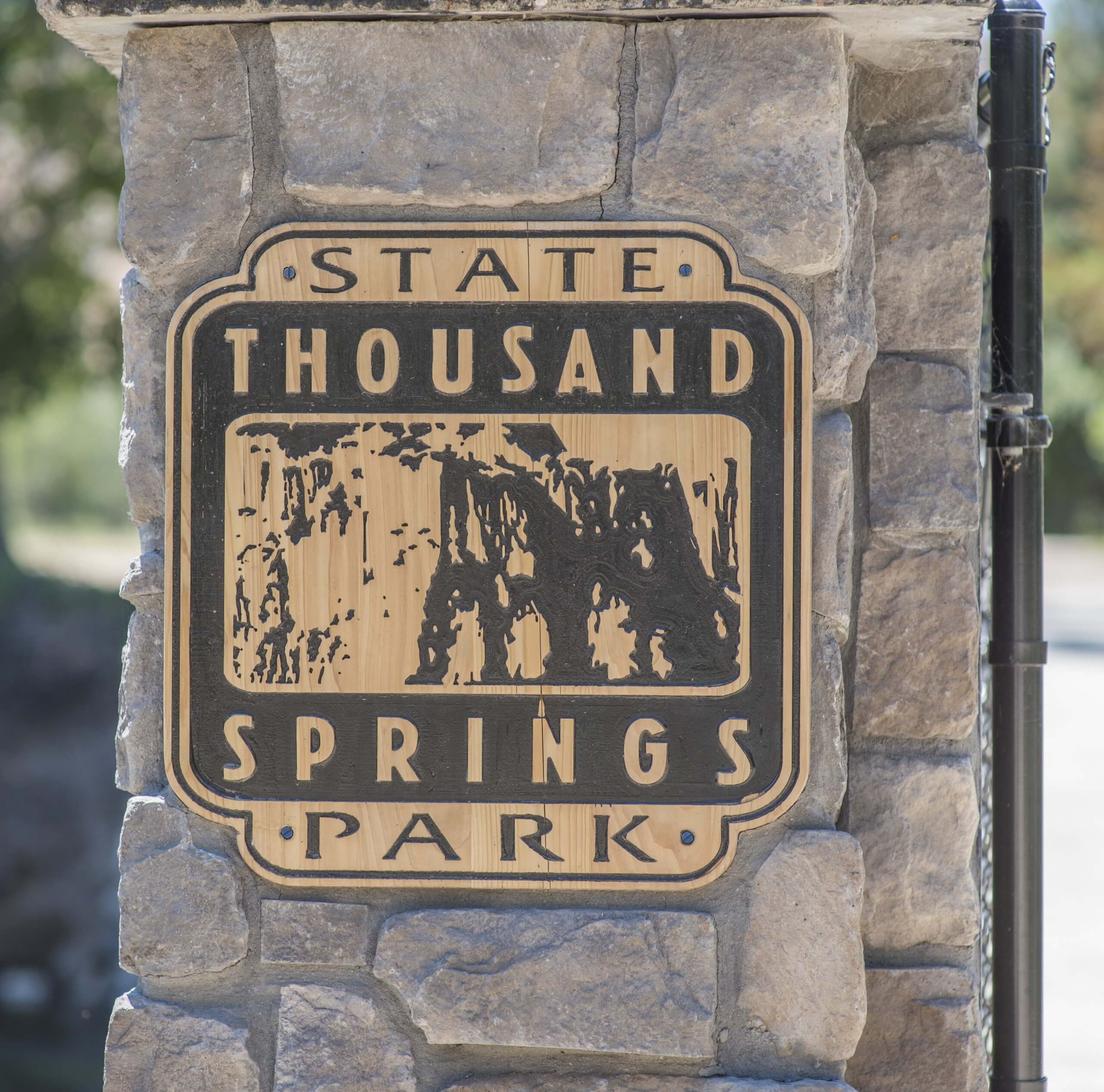Close-up of a wooden sign on a brick wall that reads "Thousand Springs State Park."