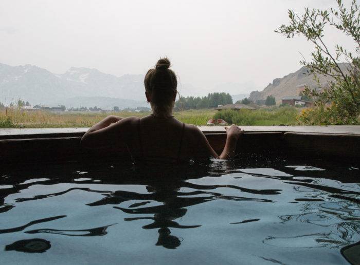 A woman looks out over a mountain range from the comfort of a hot springs tub. 