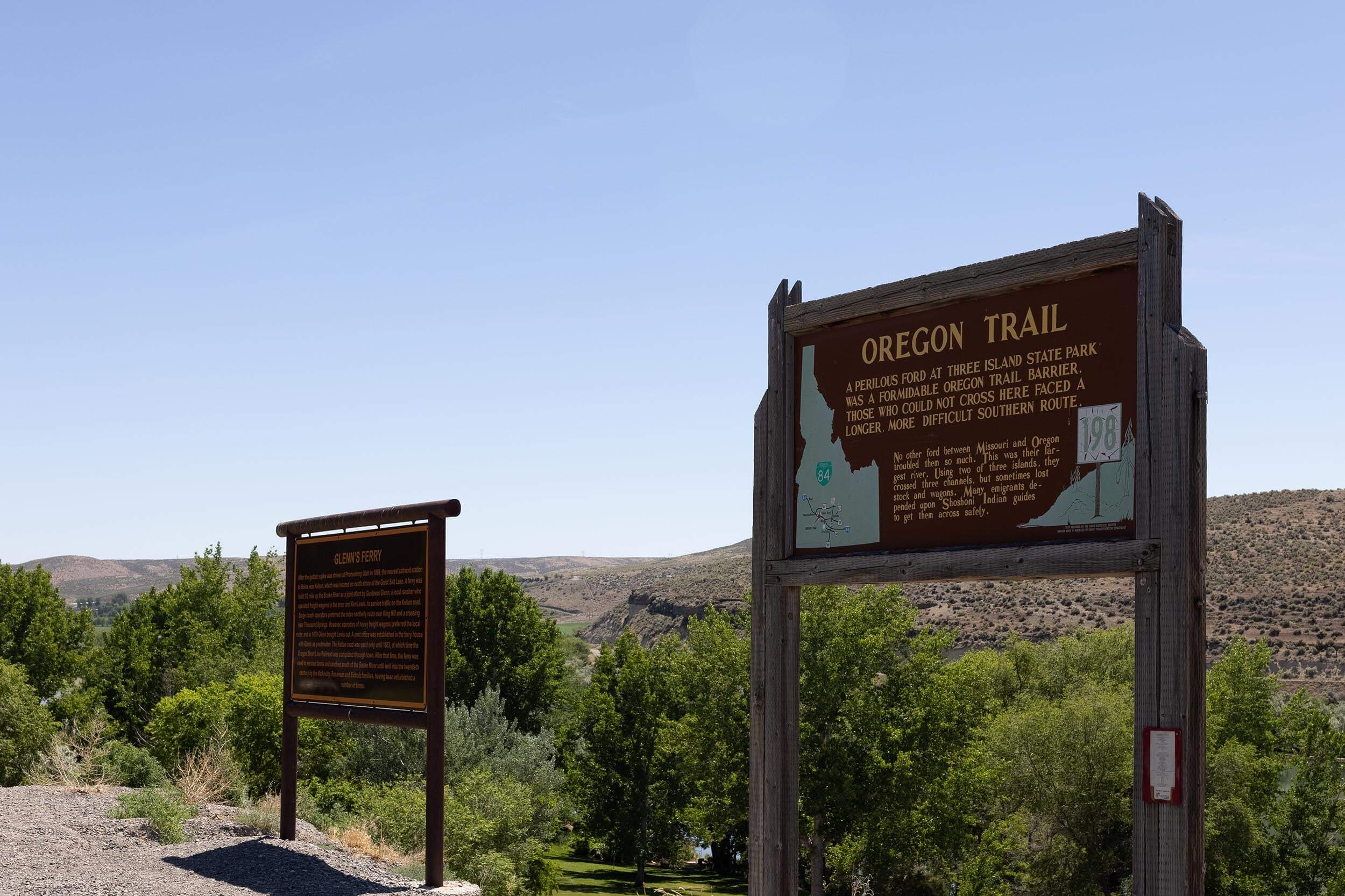 two wooden oregon trail signs in front of some shrubs with mountains in the background