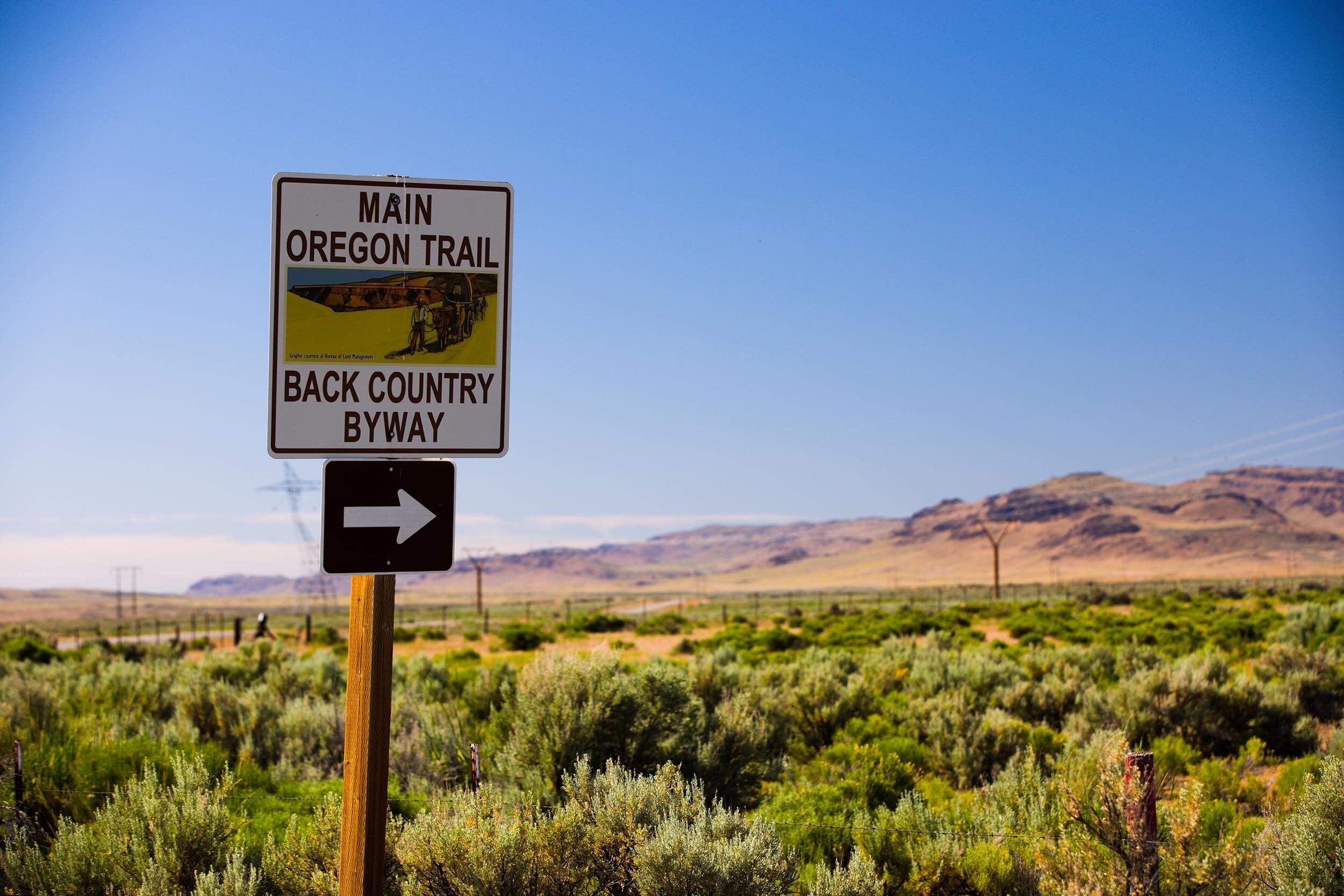 main oregon trail backcountry byway sign beside a field of desert shrubs with mountains in the distance