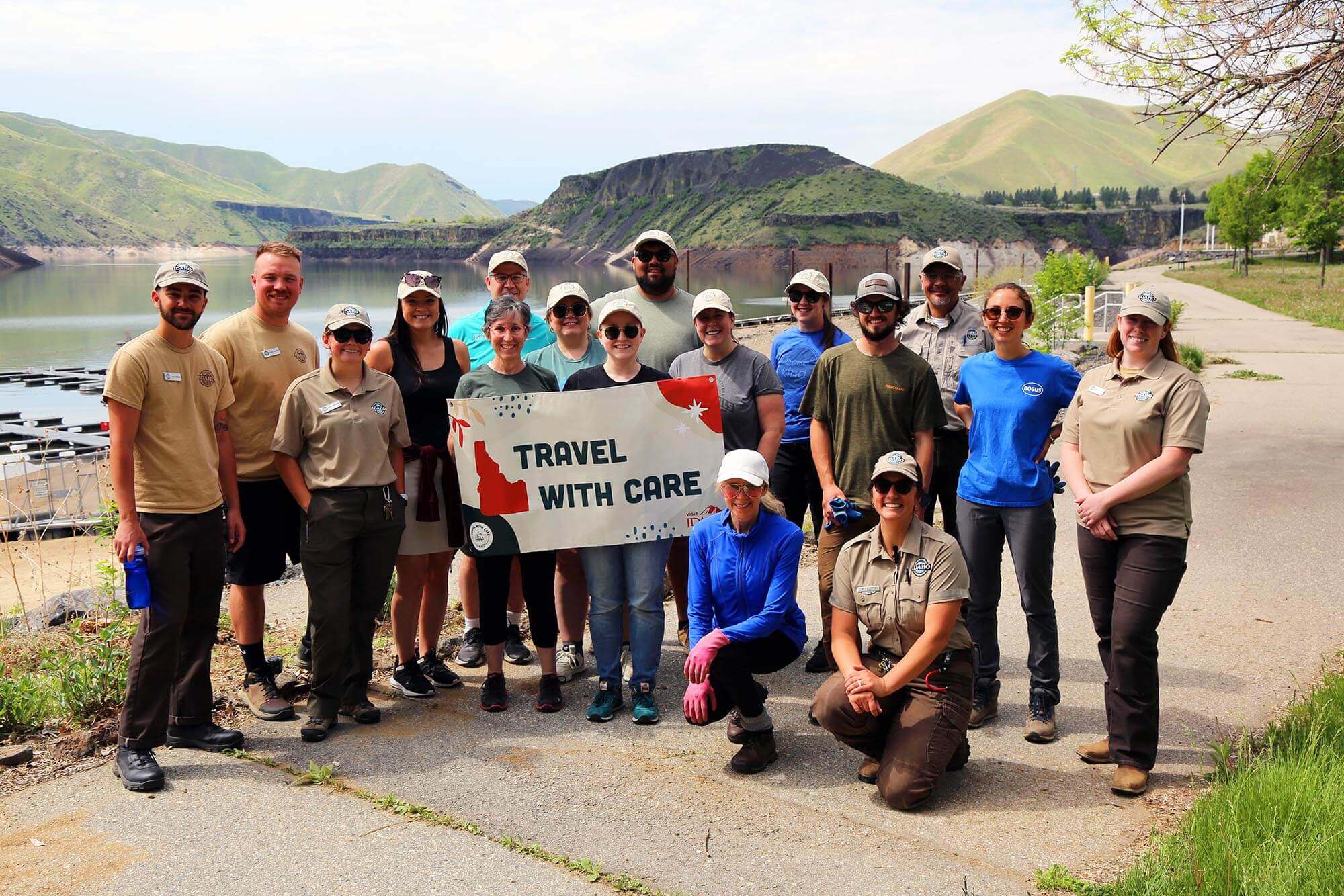 A group of volunteers posing for a photo at a Travel With Care event holding a sign reading "Travel With Care."