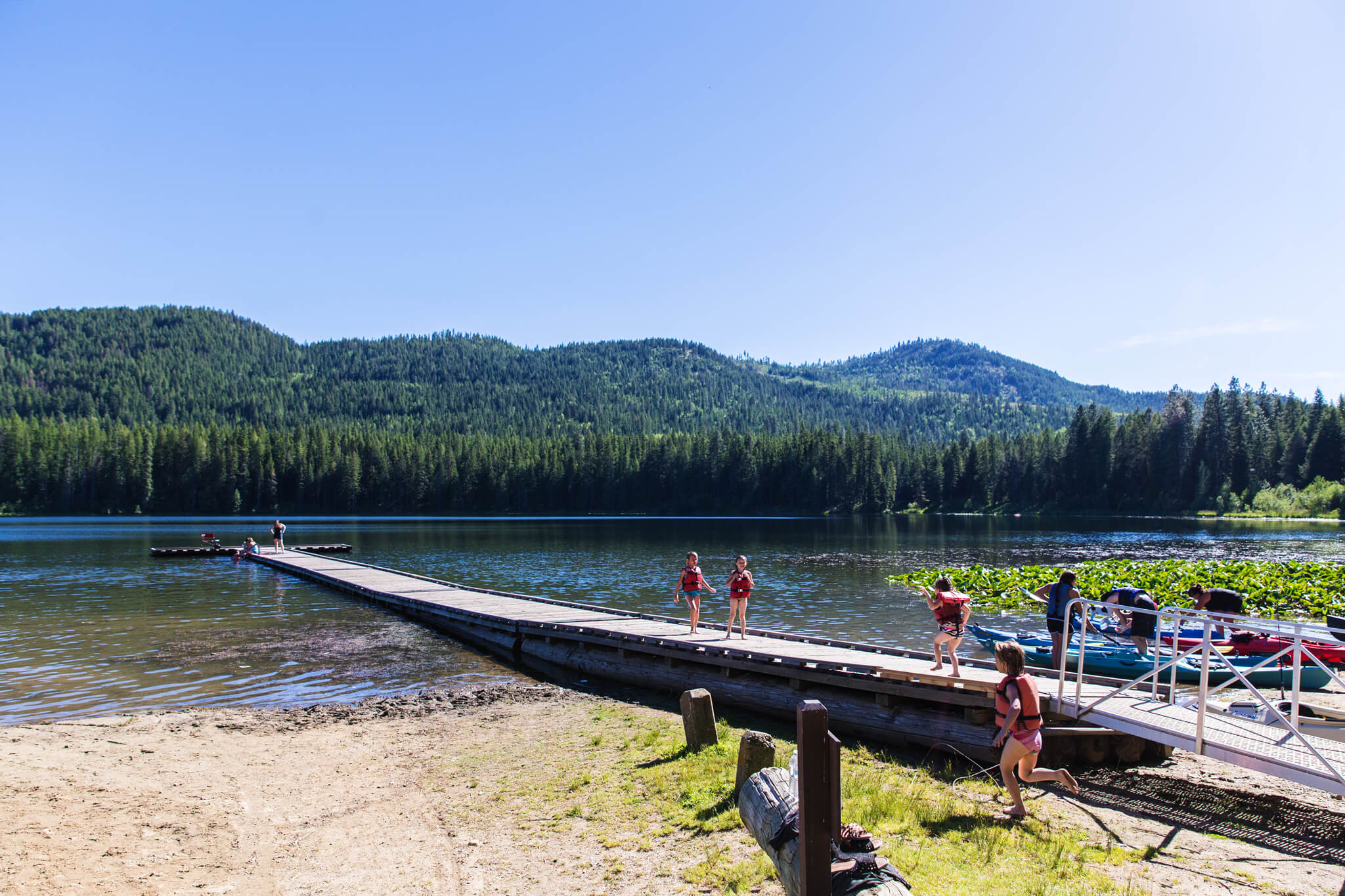 A group of people on a pier preparing to launch canoes at Round Lake, and a large forest in the background.