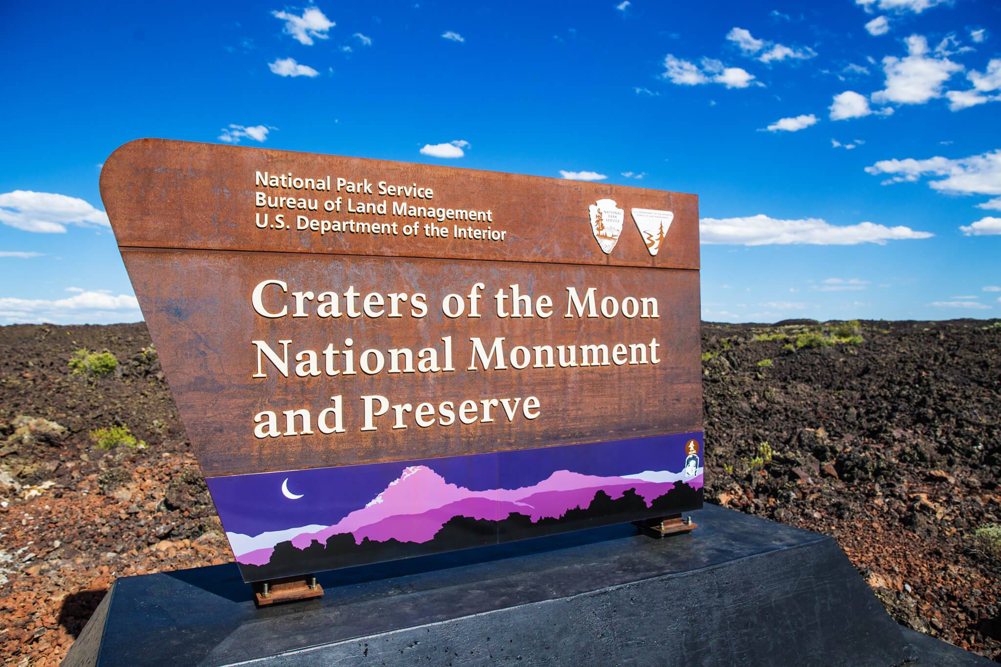 Craters of the Moon National Monument and Preserve signage at entrance of the park with a dark sky illustration at the bottom.