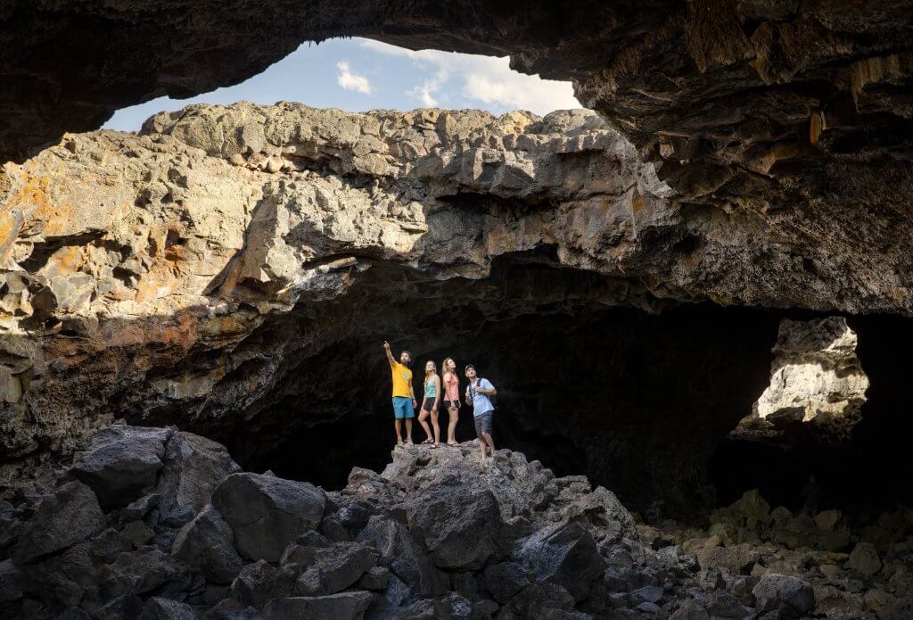 Four people inside a lava tunnel looking up toward the sky through an opening at Craters of the Moon National Monument and Preserve.