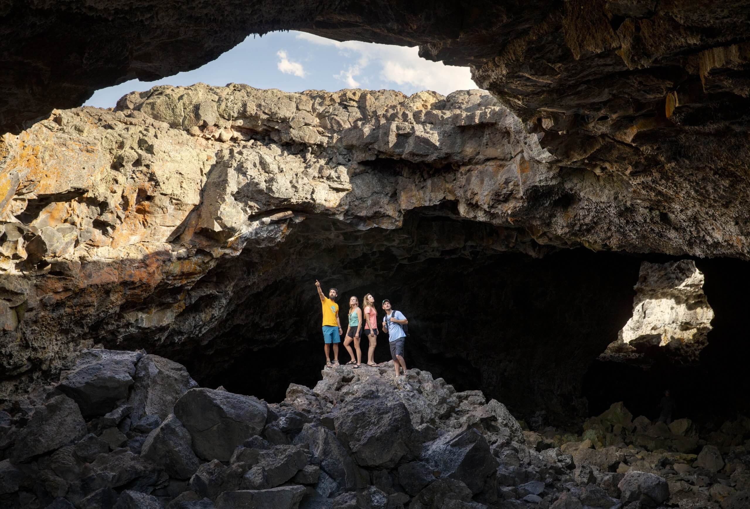 Four people inside a lava tunnel looking up toward the sky through an opening at Craters of the Moon National Monument and Preserve.
