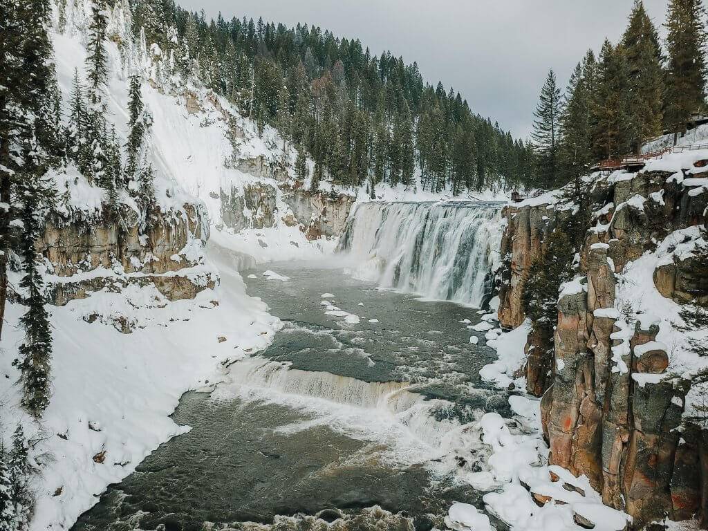 aerial view of massive Upper Mesa Falls flowing over snowy rocks and snowy riverbanks