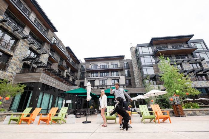 Two people on an outdoor patio with a dog in front of a hotel. 