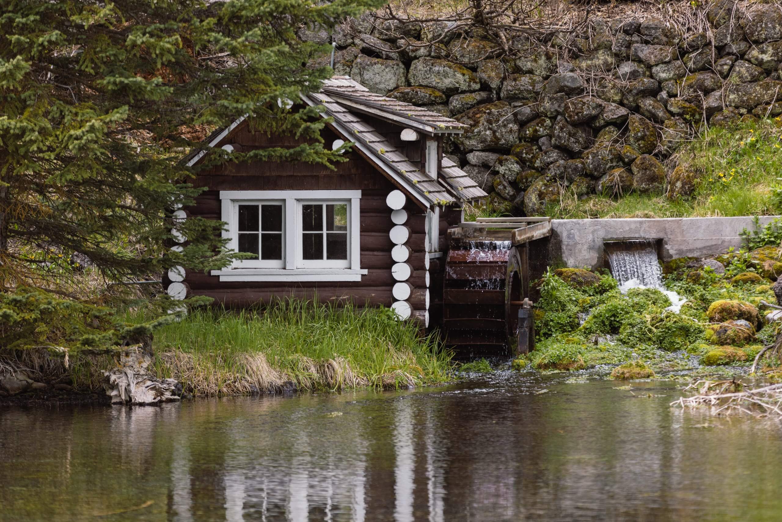An old log cabin with a water wheel next to a stream.