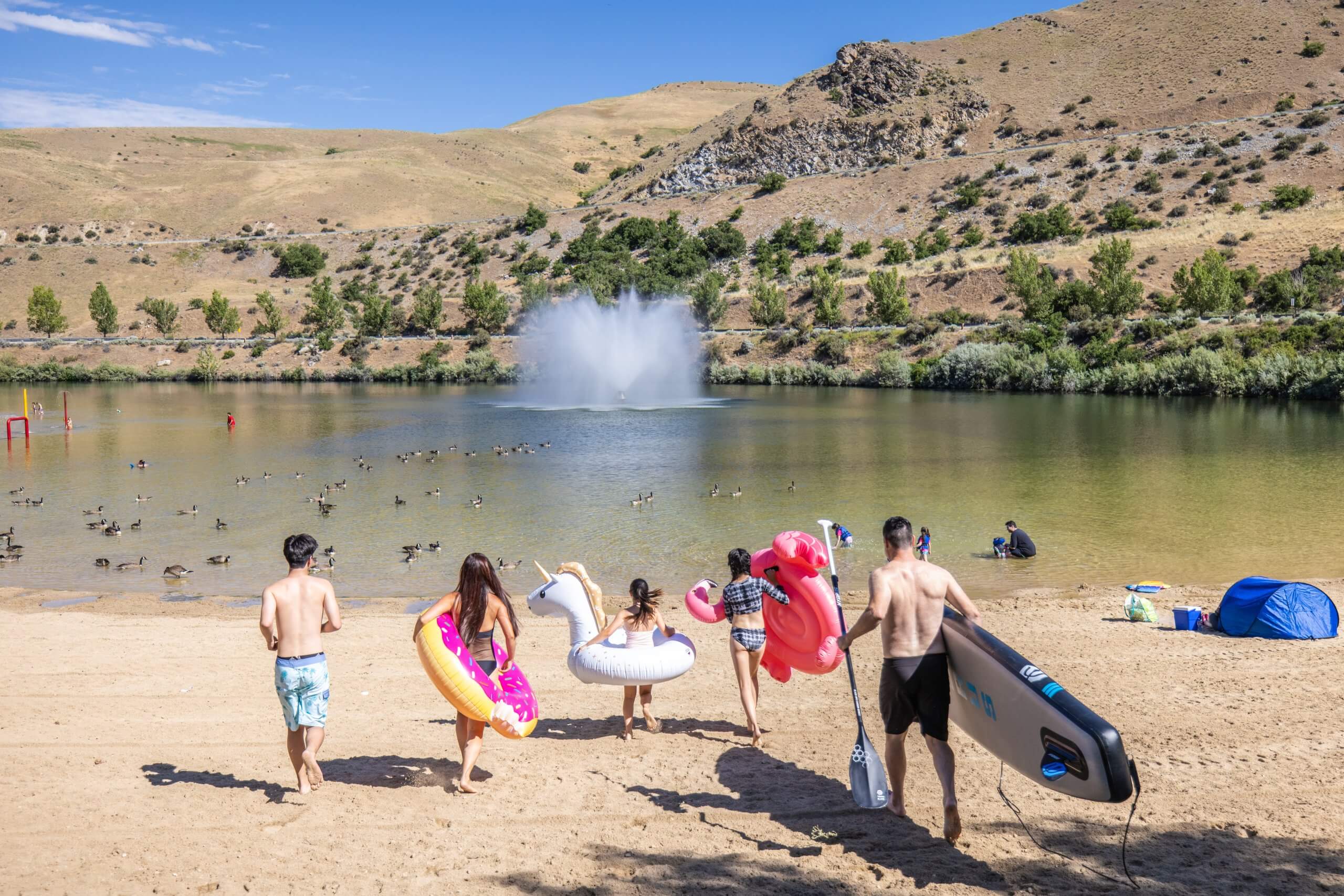A family carrying floaties running in the sand toward the water at Sandy Point Beach in Lucky Peak State Park.
