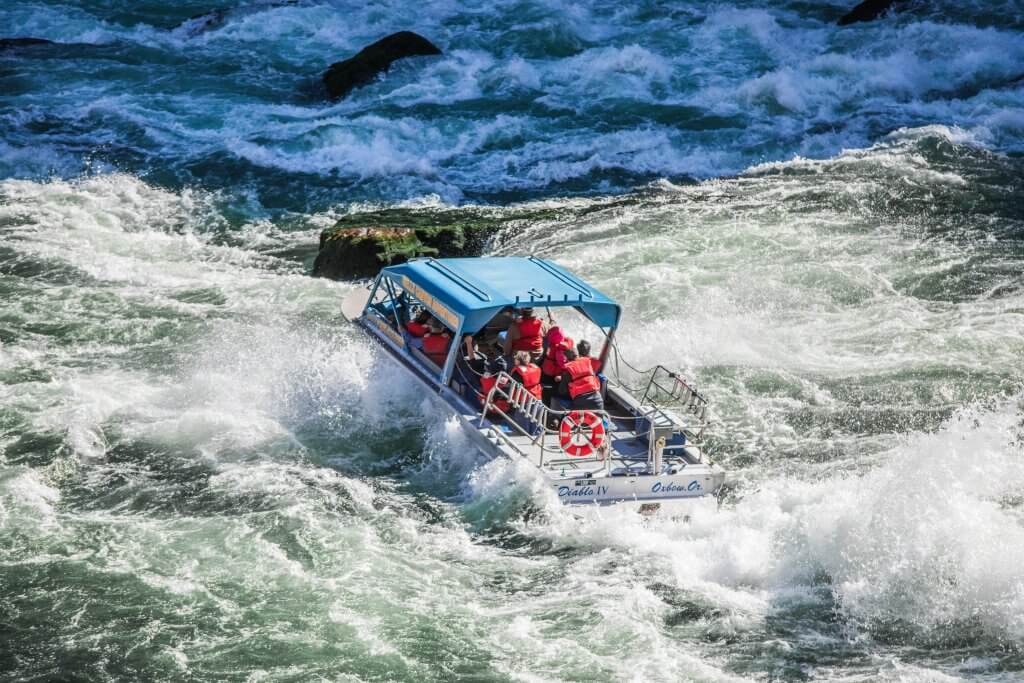 A jet boat cruises down a river, surrounded by white water