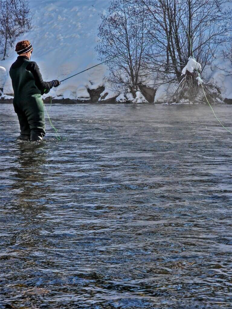 A person dressed in waders casts a line in the Henrys Fork during winter.