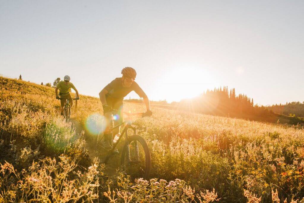 mountain bikers on trail in field at sunset