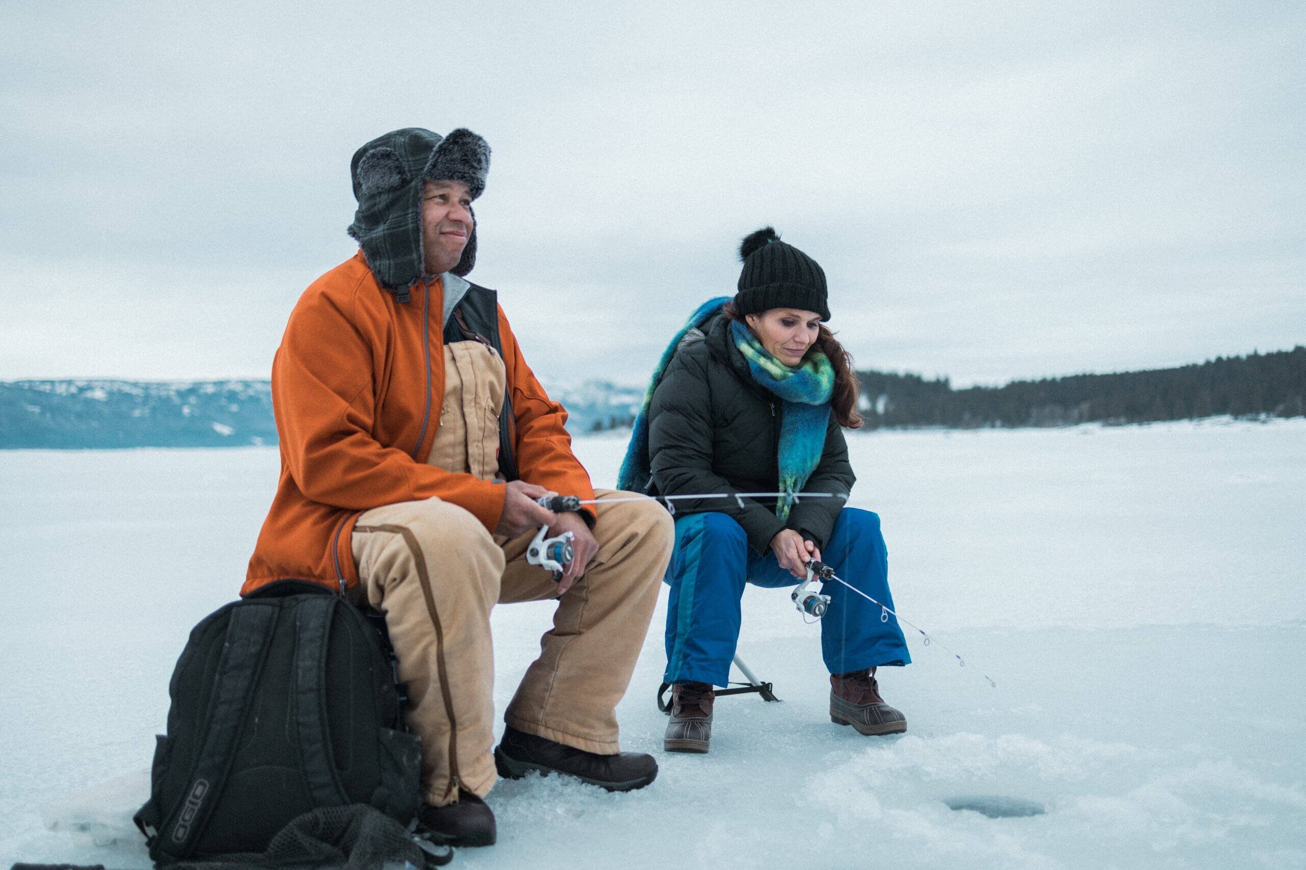 Two people sit on a frozen Lake Cascade while ice fishing.