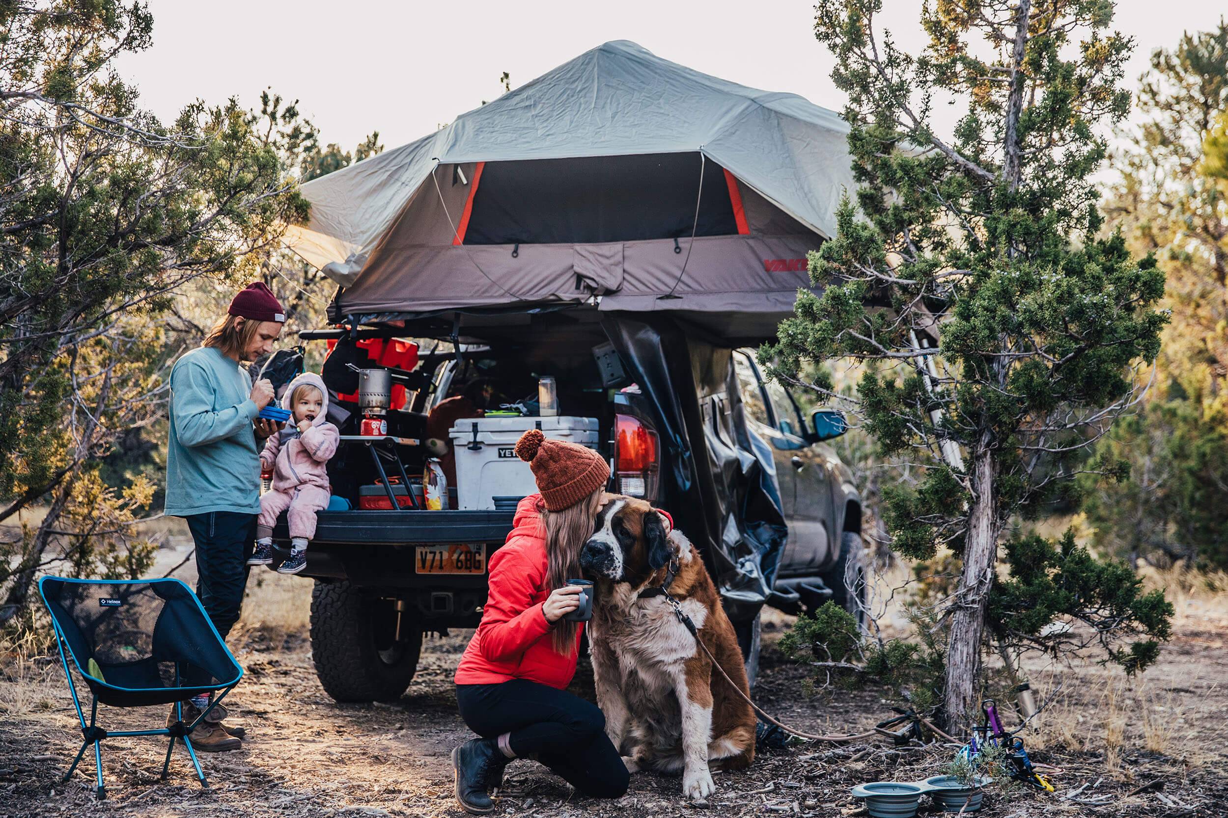 A family of three with a dog outside behind a truck with a rooftop tent at Smoky Mountain Campground.