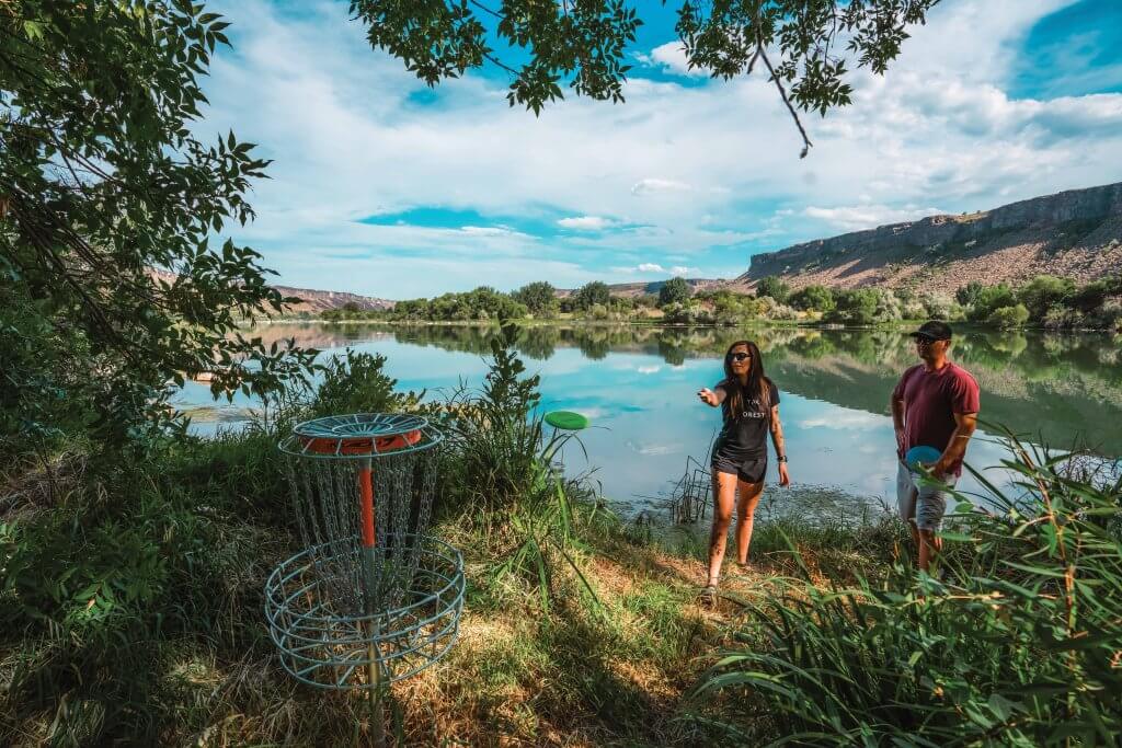 Two people playing disc golf with a lake in the background at the Niagara Springs unit of Thousand Springs State Park.