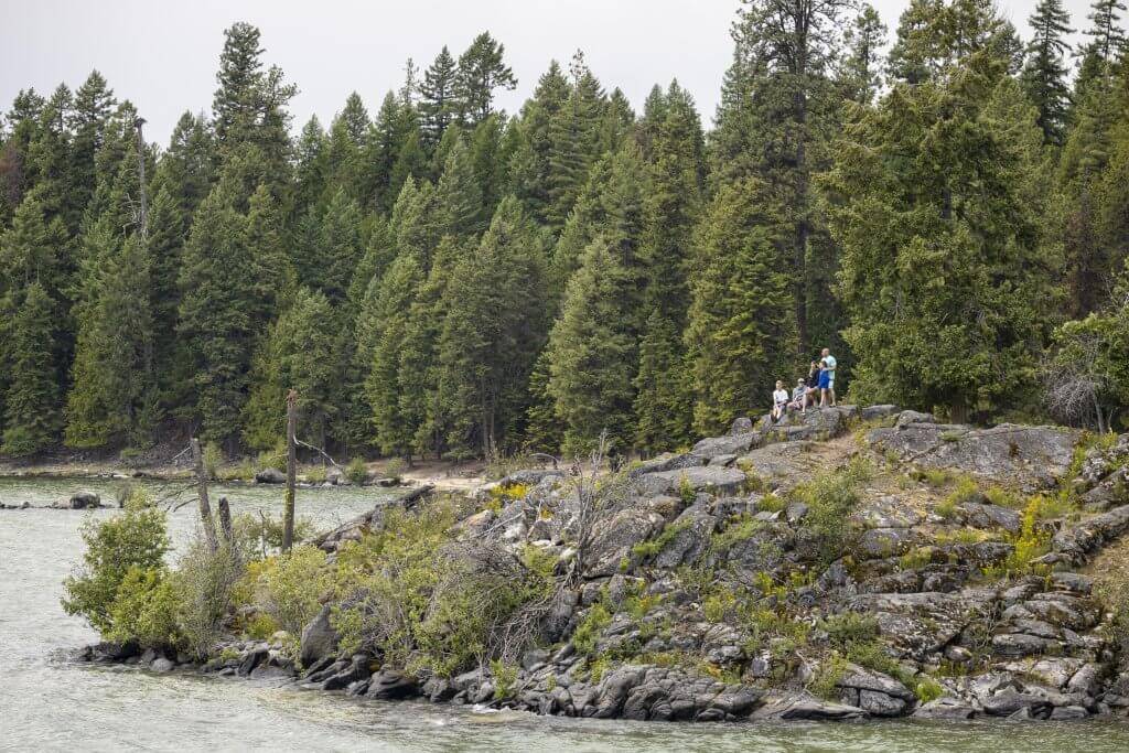 People standing on rocks overlooking Priest Lake with trees in the background.
