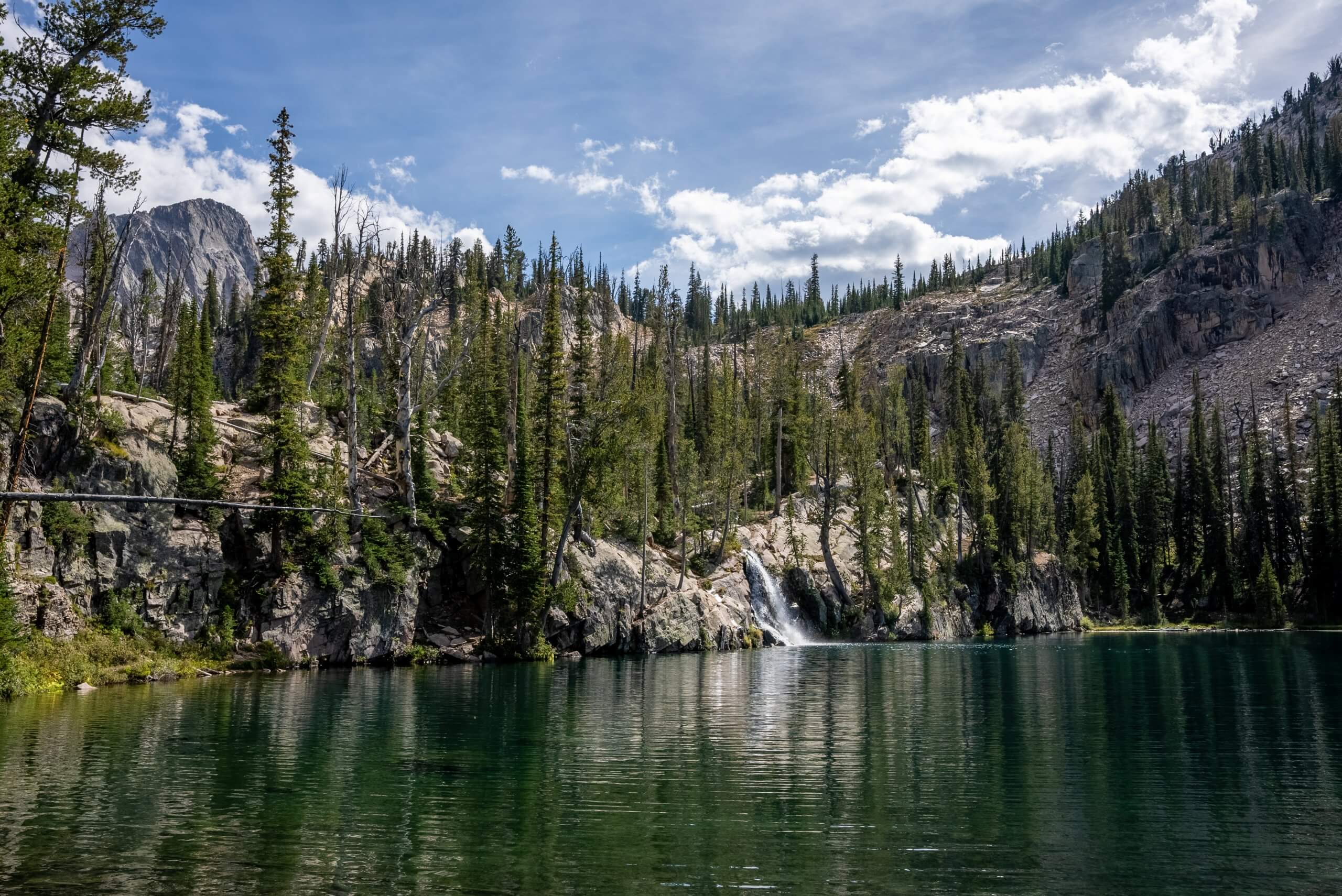 A view of Middle Cramer Lake surrounded by tree-covered mountains in the Sawtooth Wilderness.