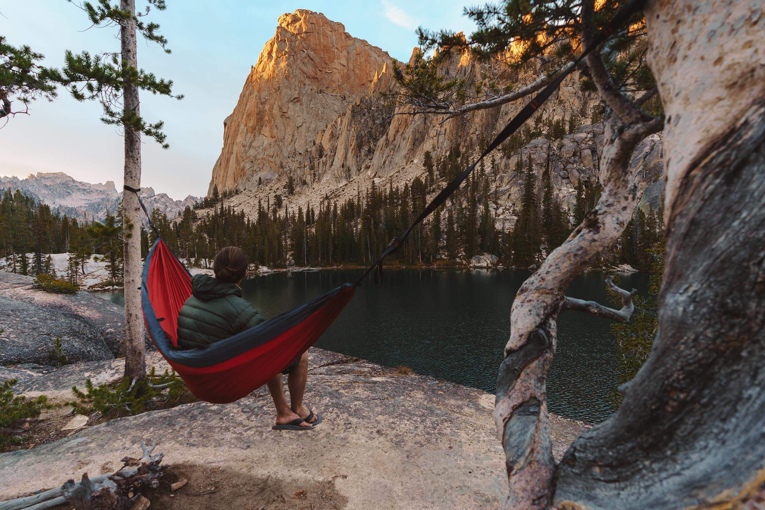 a man sits on a red hammock looking at the Elephant's Perch in the Sawtooth Mountains