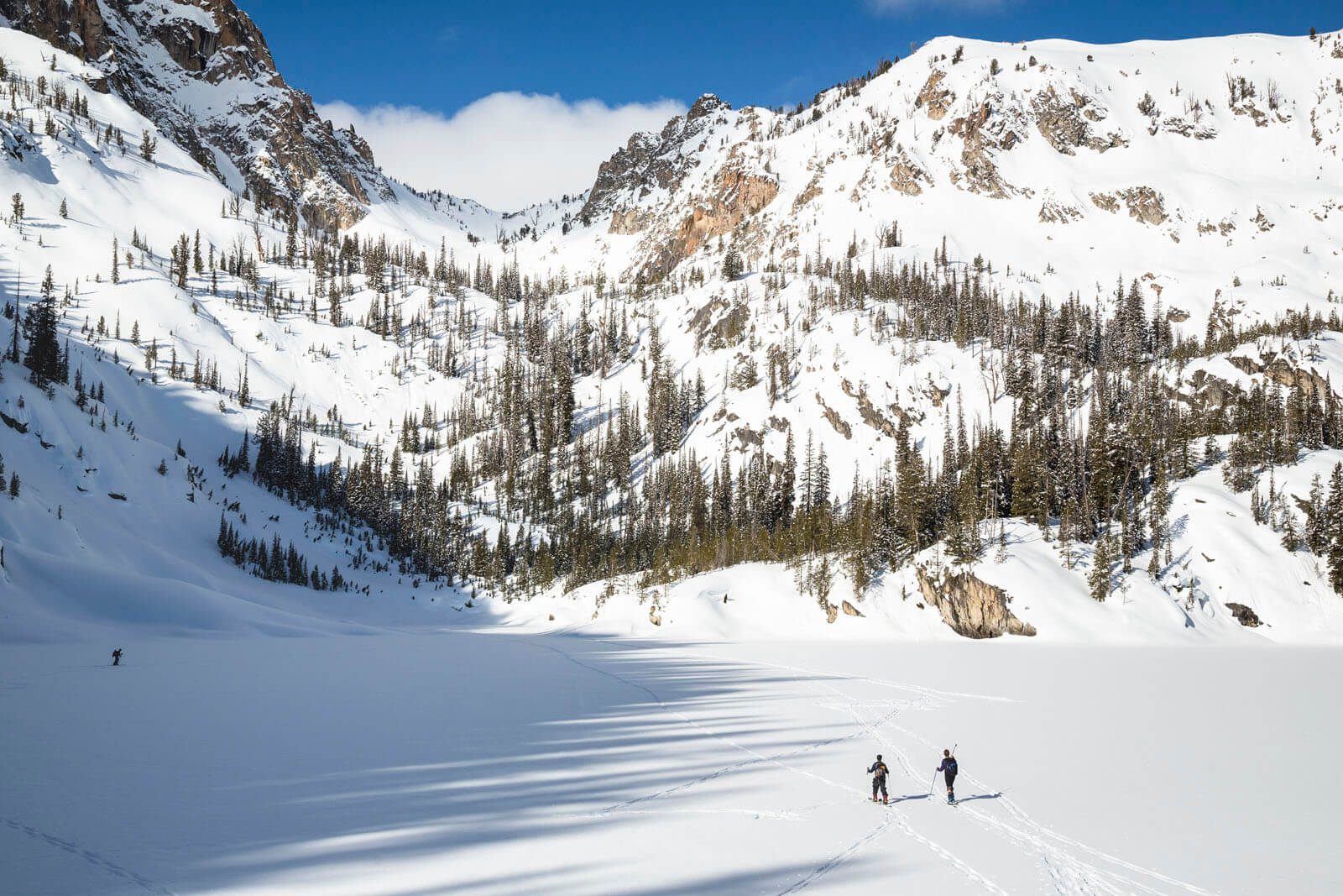 Two people in ski and snow gear backcountry ski in the Sawtooth Mountains, near Stanley. 