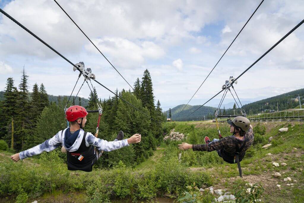 Two people ziplining over forested area.
