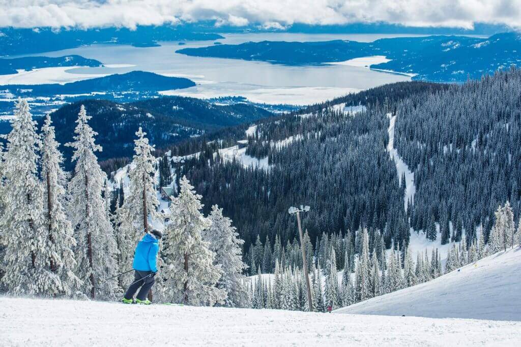 a person in blue skis atop a mountain peak at Schweitzer