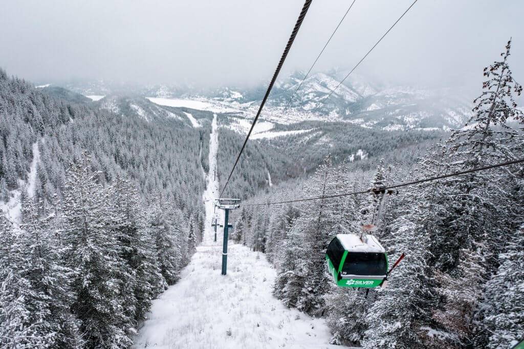A green gondola going down a cable on a snowcovered mountain.