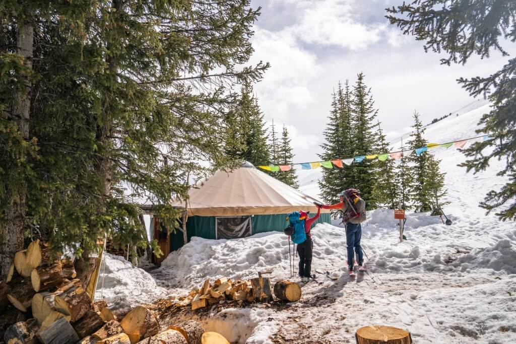 Two hikers in snow gear high-five outside of the Pioneer Yurt during winter.