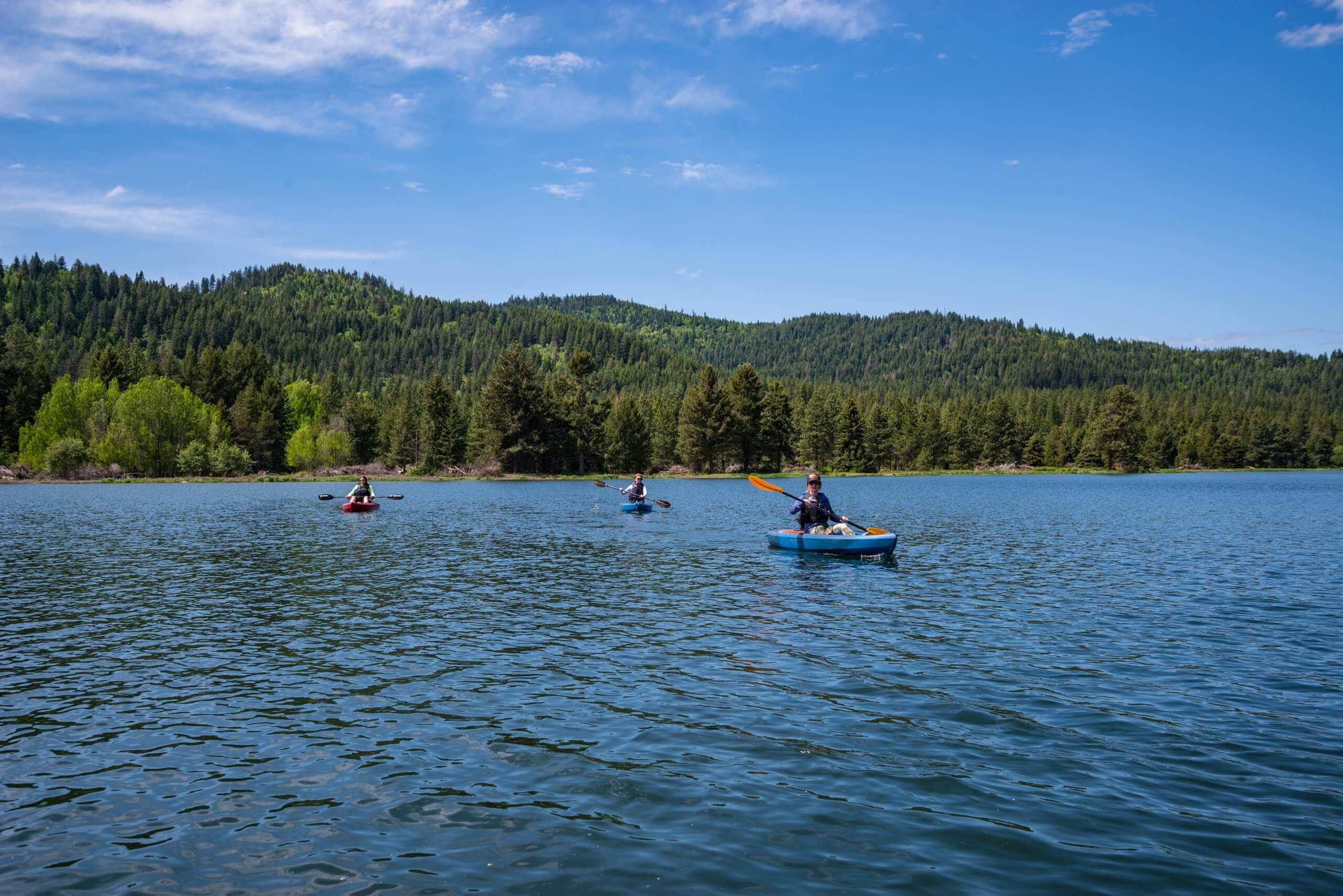 three people kayaking at Spirit Lake, with tree-covered hills in the background
