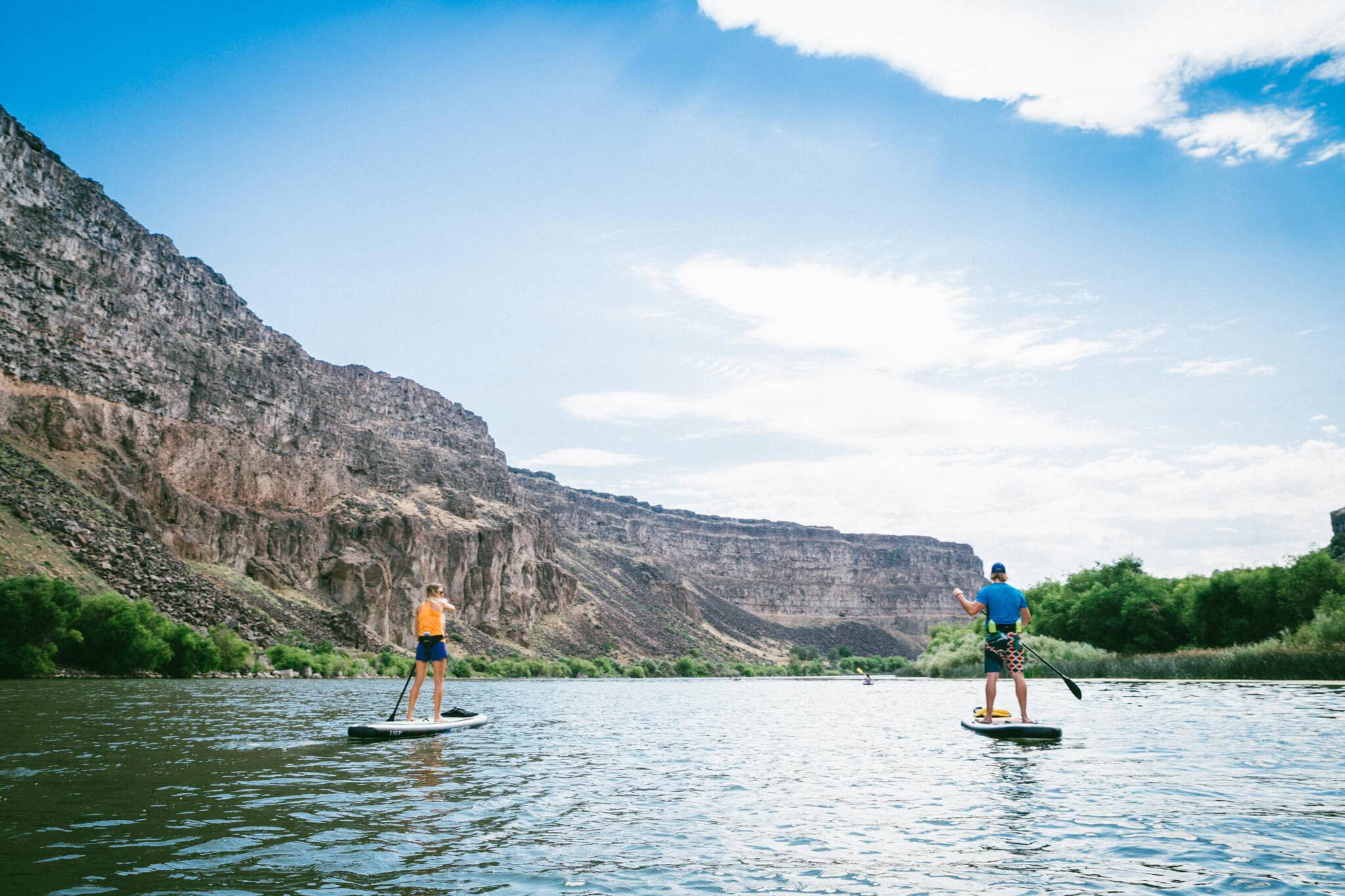 Two people stand up paddleboarding on the Snake River past a rugged landscape.