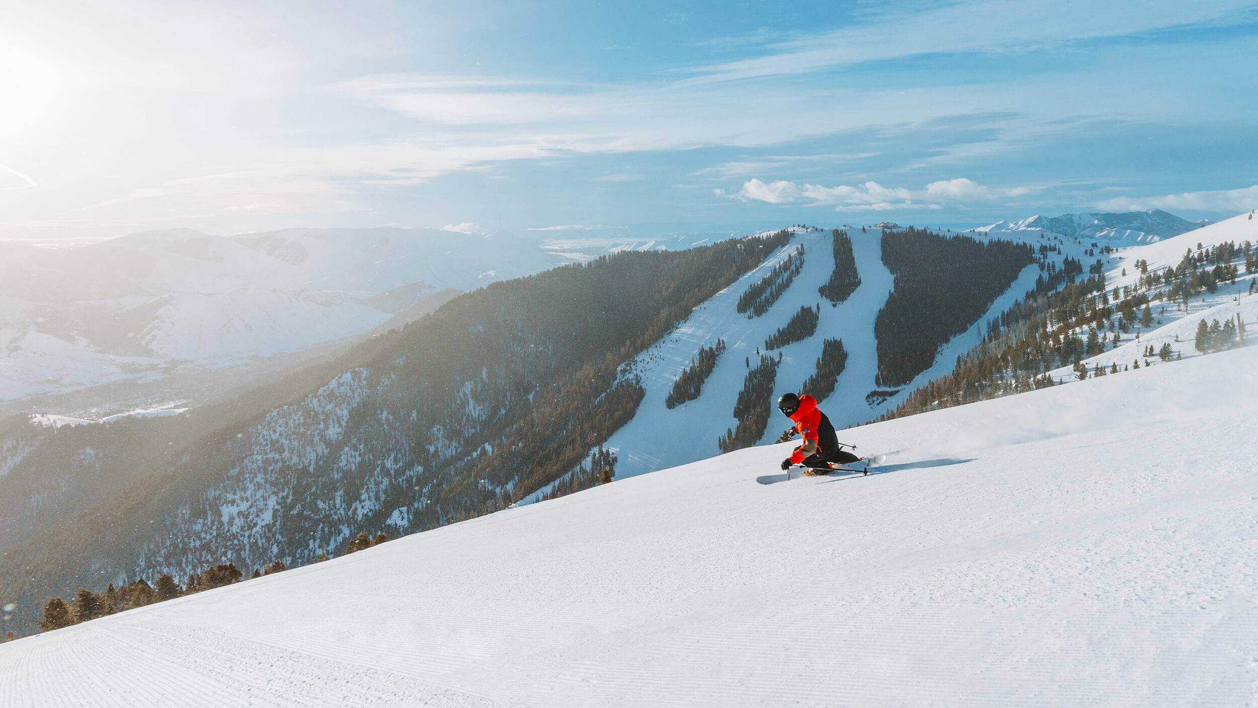 A skier in red glides down an expansive slope in Sun Valley