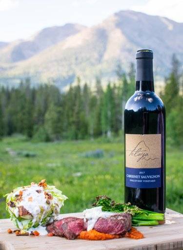steak, salad and bottle of wine with mountain in background