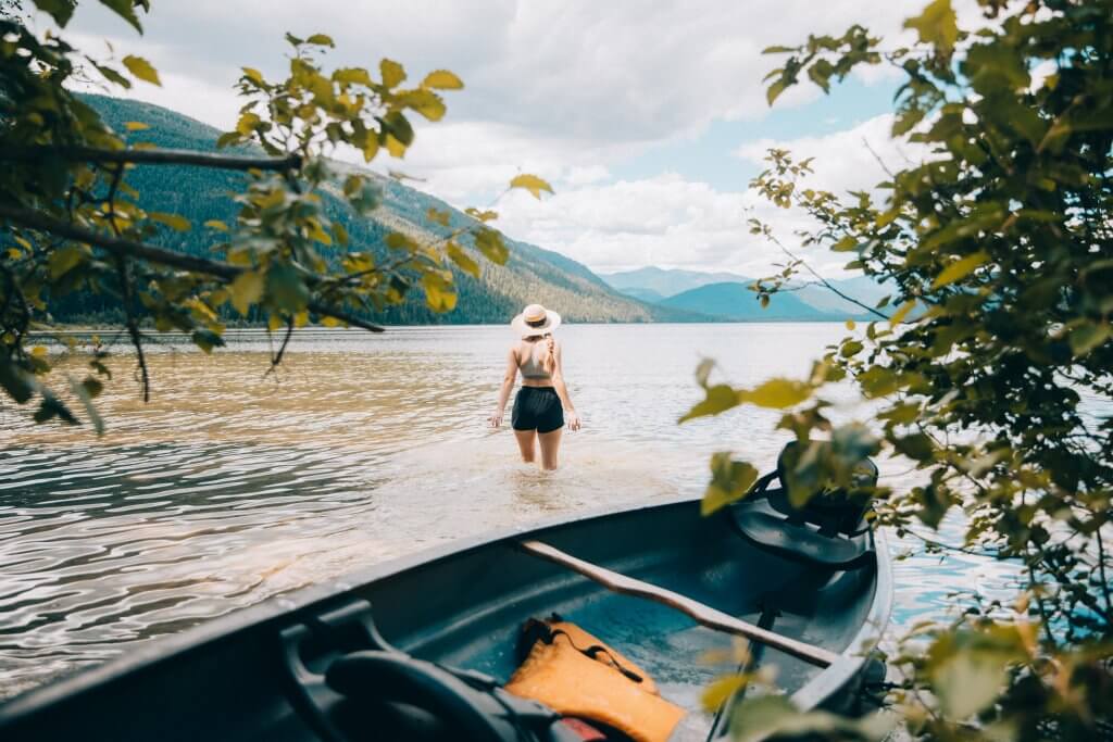 Woman standing in lake water in front of a canoe facing view of mountains.