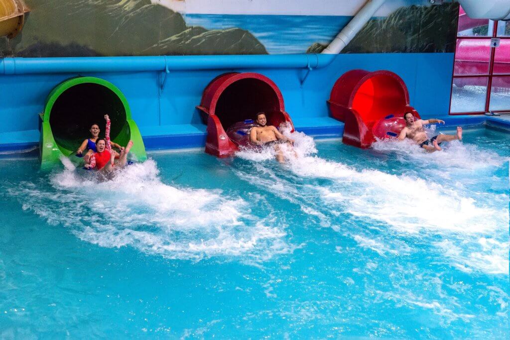 Water park visitors splashing into a pool of water from three waterslides.
