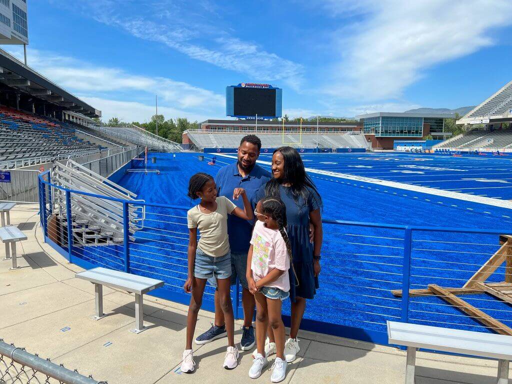 a family of four standing in front of the blue turf of the Boise State Broncos