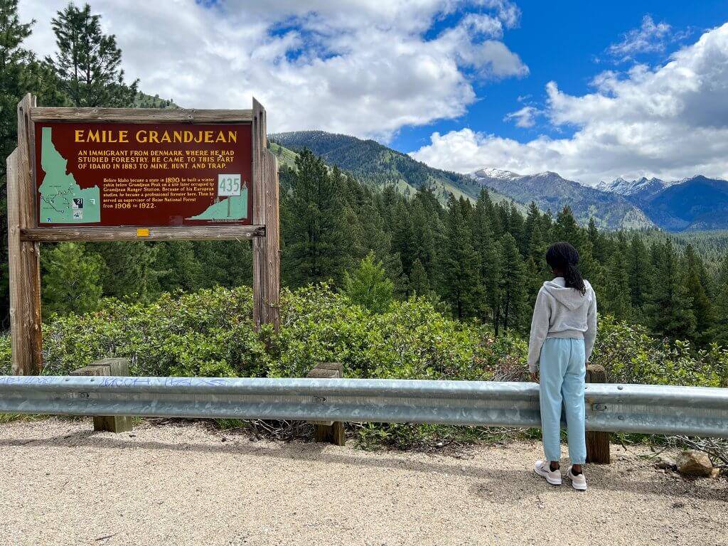 girl  standing at scenic overlook with historical sign to the left and sweeping mountain views in the distance
