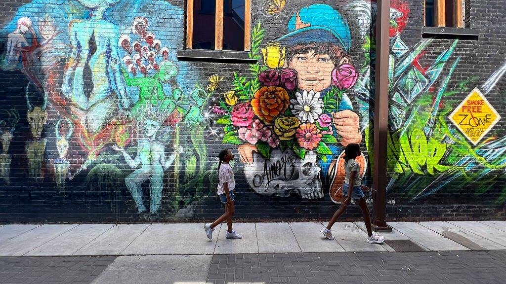 two girls walk by tall brick wall with vibrant painted murals.