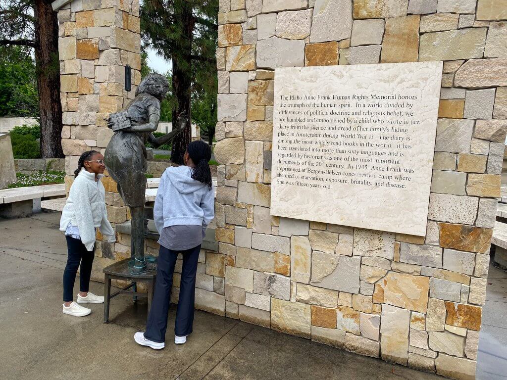 two young girls standing next to a statue of Anne Frank at the Idaho Anne Frank Human Rights Memorial