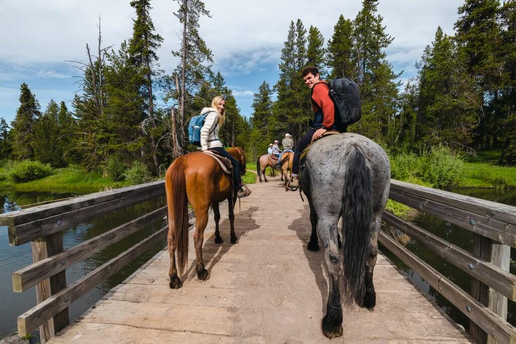 a man and a woman sitting on horses. the woman is on a brown horse and the man on a gray horse, walking across a wooden bridge in Harriman State Park.