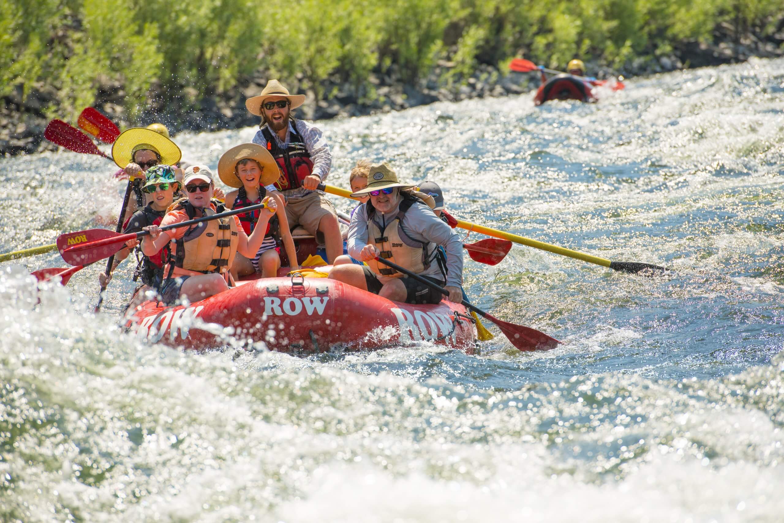People holding paddles on a red raft navigate through white water in the Lower Salmon Canyon.