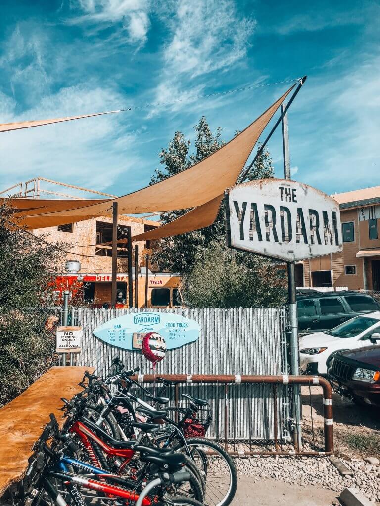 Exterior of Yardarm showing a sun shade hanging over a dining area with a line of bikes hooked up to a bike rack.